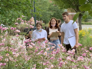 Students holding clipboards look at pink flowers